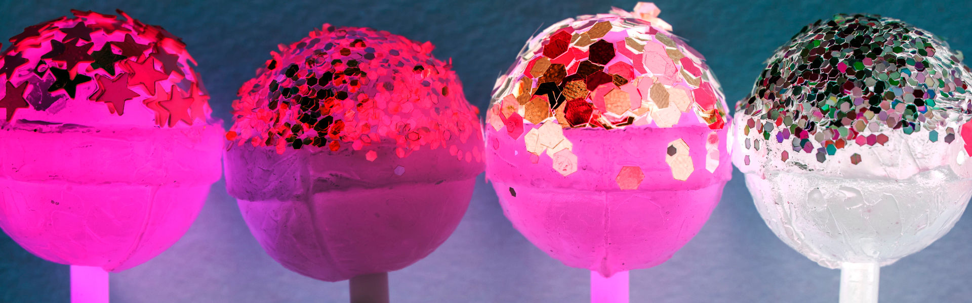Four lollipops covered in sugary glitter. Colours are similar to those of the bisexual flag.
