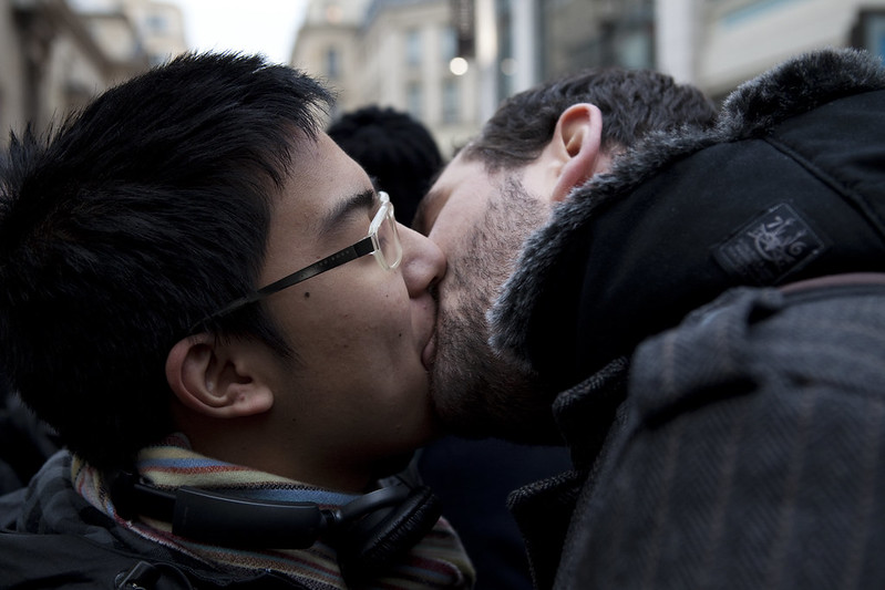 Two guys kissing outdoors in a crowd, at what seems to be a kiss-in.