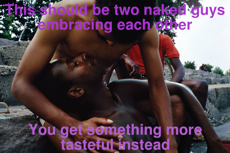 Two shirtless men embracing each other tenderly, outdoors in public. They are sitting on a rock outcropping and there are other people hanging around. Captions overlay the image that read, "This should be two naked guys embracing each other. You get something more tasteful instead."